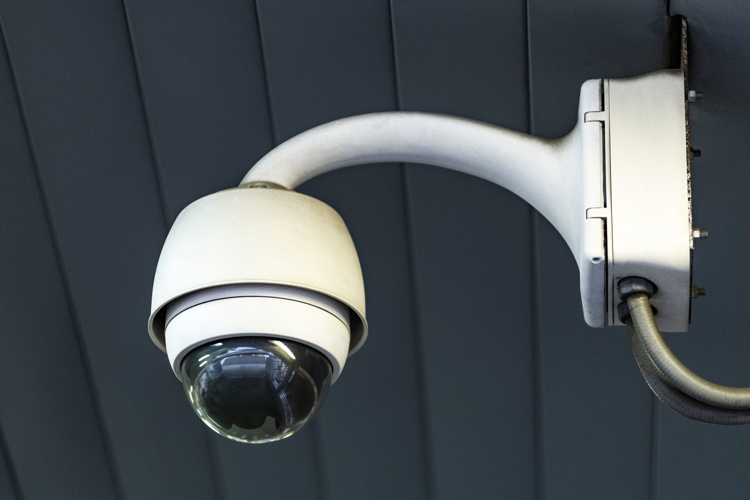 White dome surveillance camera installed on exterior wall under roof overhang