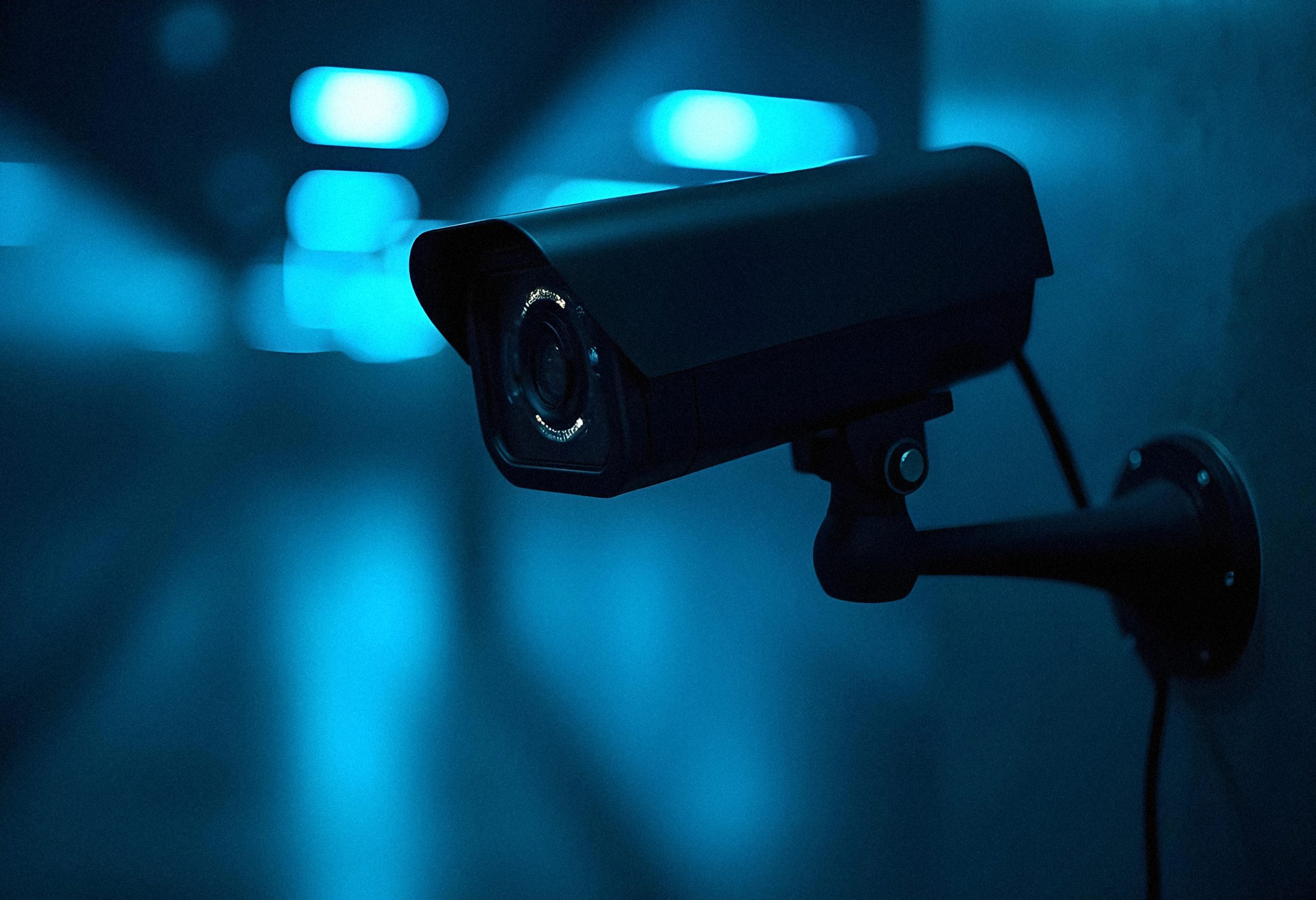 Close-up of a wall-mounted security camera in blue lighting at night